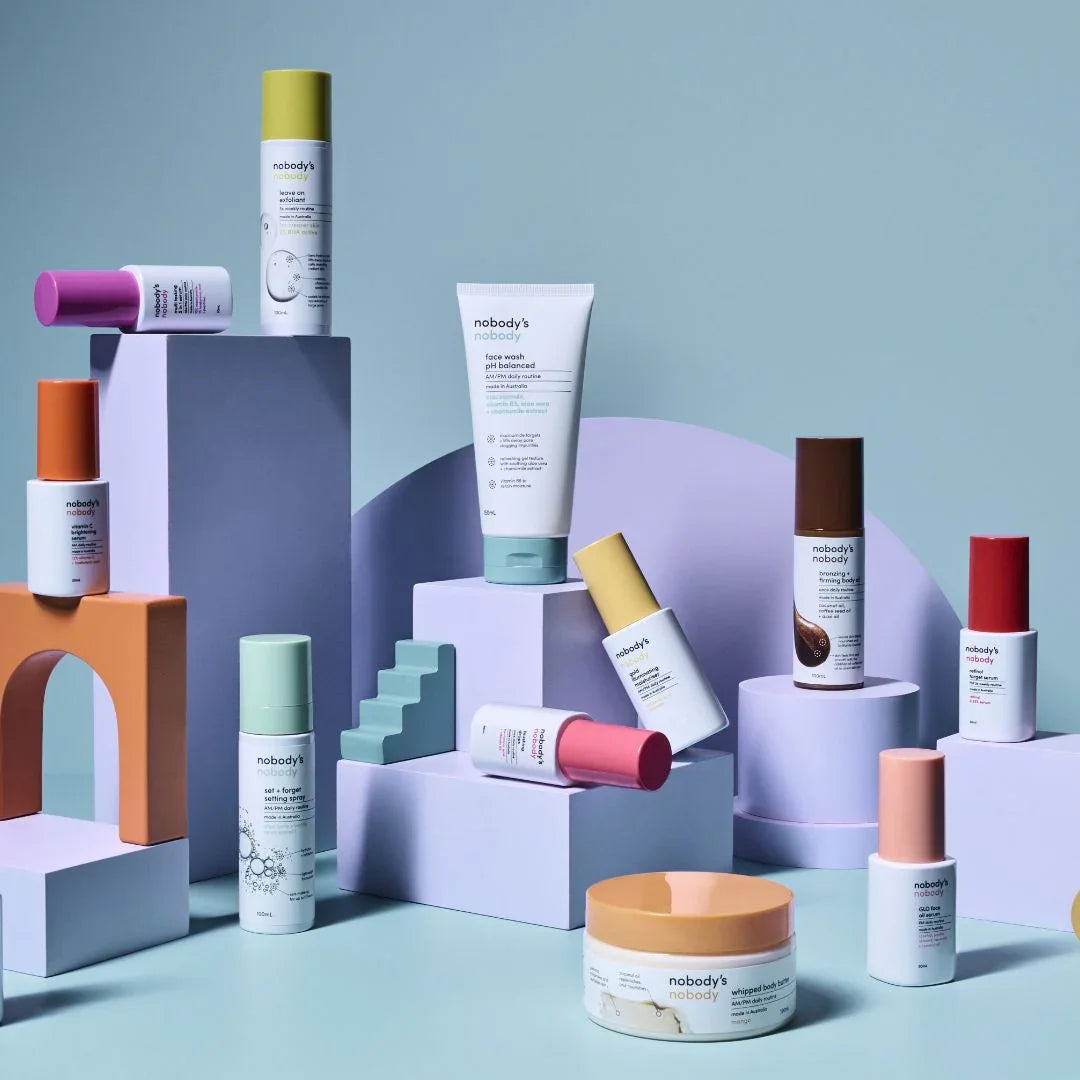 Nobody's Nobody skincare products arranged on pastel geometric stands, minimalist background